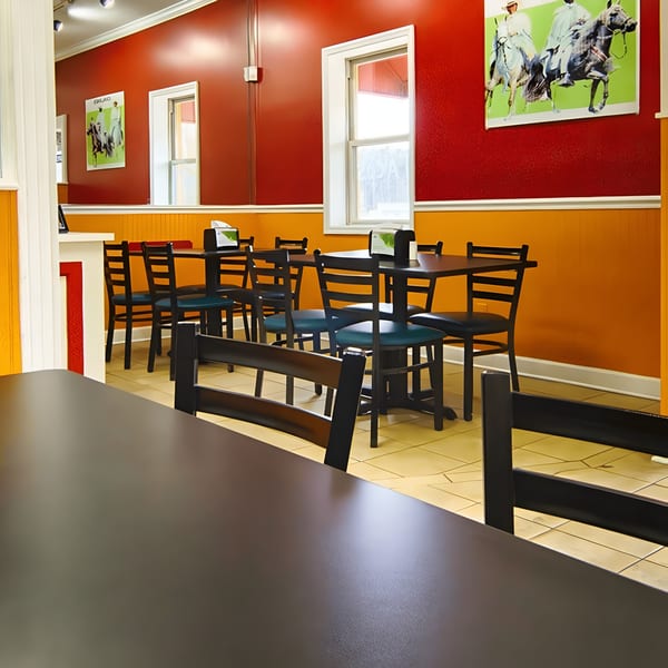 Interior of MMM Que Rico with red and orange walls, black tables, and chairs, featuring Latin-American art.