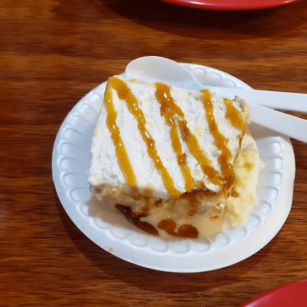 A slice of tres leches cake with caramel drizzle and a white spoon on a white plate.