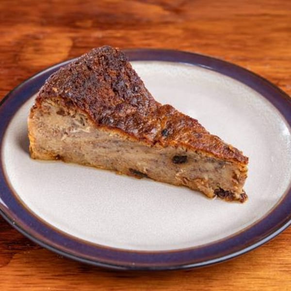 A slice of Latin-American bread pudding with raisins on a white plate with a blue rim.