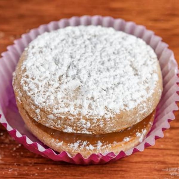 A Latin-American alfajor cookie with dulce de leche filling and powdered sugar, in a pink paper cup.