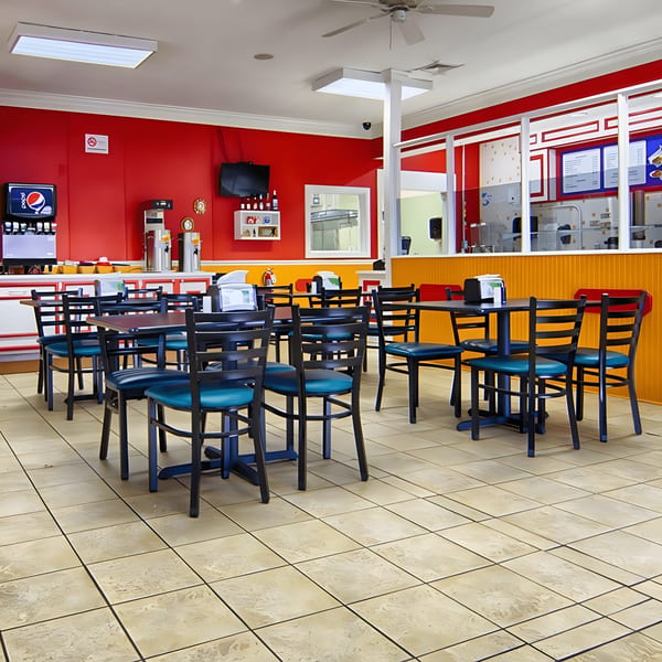 Empty dining area of MMM Que Rico with red and yellow walls, black tables, and teal chairs.