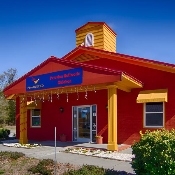 The vibrant red and yellow exterior of MMM Que Rico, a Peruvian Rotisserie Chicken restaurant.
