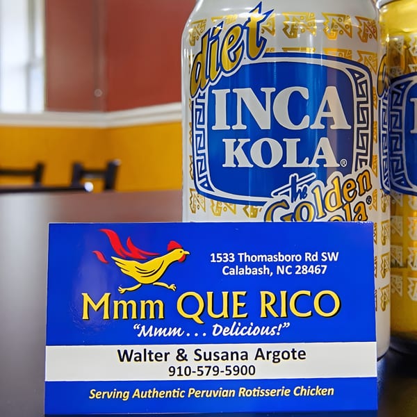 Mmm Que Rico business card in front of Diet Inca Kola cans, advertising Peruvian rotisserie chicken.