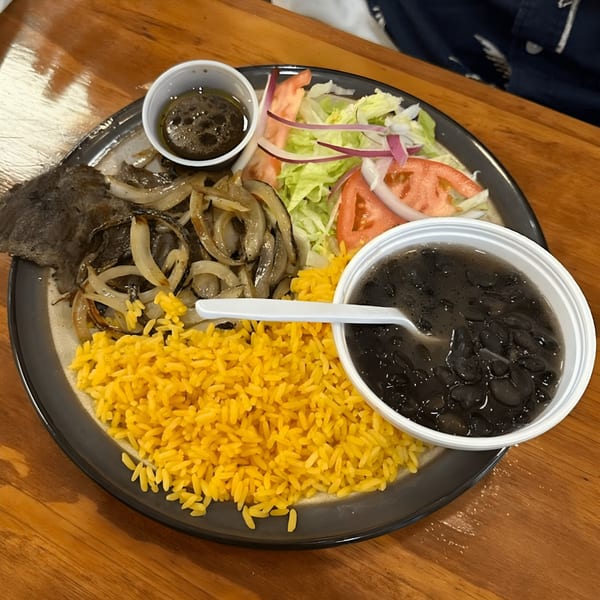 A Latin-American dish with yellow rice, black beans, steak with onions, and a side salad.