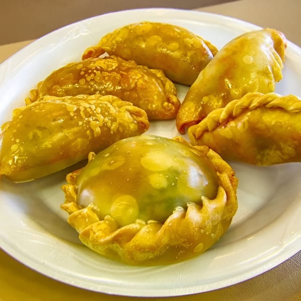 A white plate holds several golden-brown, freshly baked Latin-American empanadas from MMM Que Rico.